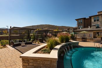 A pool with a waterfall and a patio area with a table and chairs.